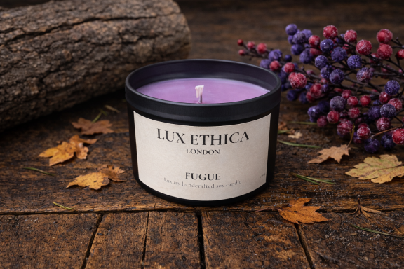Purple candle in a black container, surrounded by autumn leaves and decorative berries.