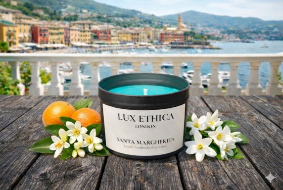 A turquoise candle beside oranges and white flowers with a coastal town backdrop.